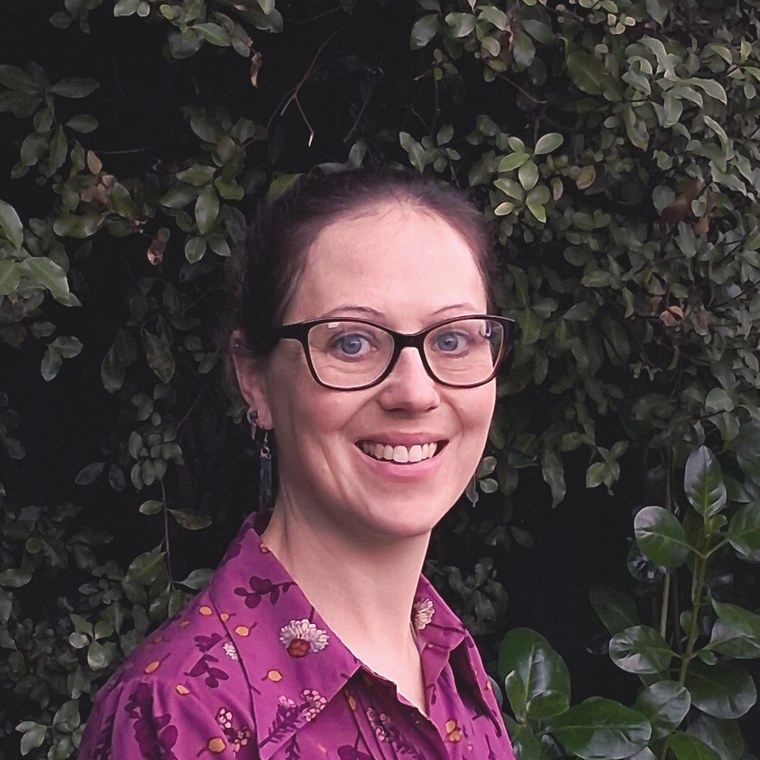 Jo Dangerfield, arts psychotherapist, smiling in front of green foliage